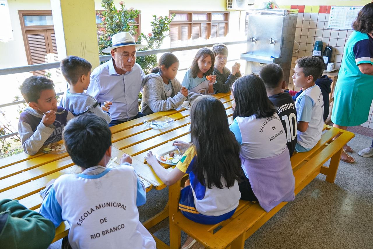 Foto do Prefeito Tião Bocalom com os alunos fazendo sua refeição